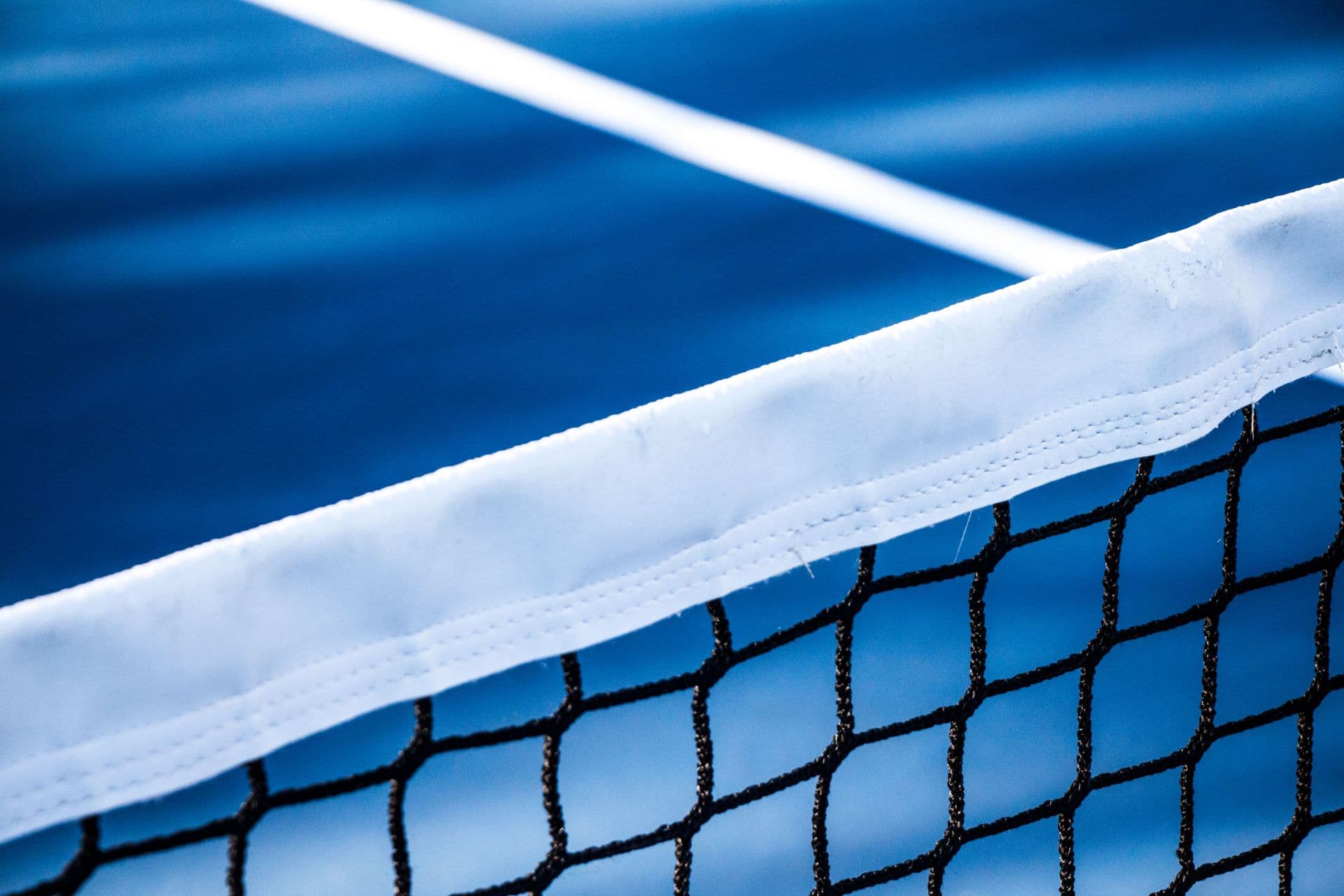 Gros plan sur la bande blanche d’un filet de pickleball, devant un terrain bleu